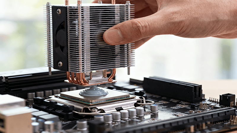 One hand carefully and vertically presses a large CPU cooler onto the CPU that has been coated with thermal grease.