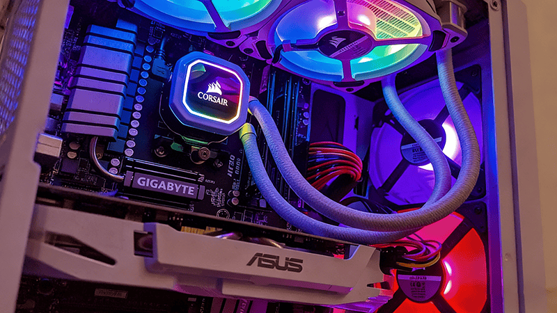 Close-up of a Corsair AIO cooler on a Gigabyte motherboard, with RGB fans and an Asus graphics card visible inside a PC case, illuminated by colorful lighting