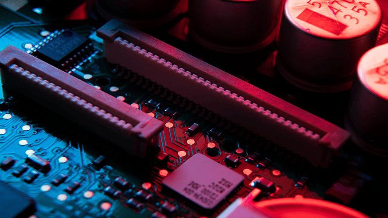Motherboard with expansion slot, capacitors and microchips (close-up, red & blue backlighting)