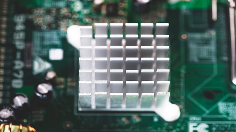 Close-up of a silver aluminum heatsink mounted on a green circuit board (motherboard), with electronic components visible in the blurred background.