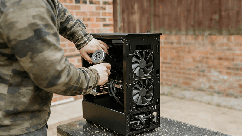 A person installing a fan into the rear of a black PC case, with two pre-installed fans visible on the side panel