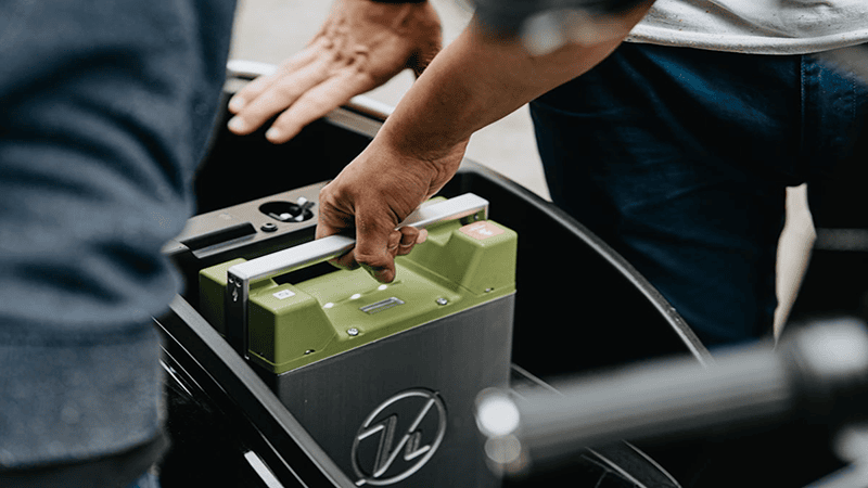 Person installing green rechargeable battery pack: Hand placing a green battery module into black equipment, suitable for electric vehicle (EV) power systems or portable energy solutions