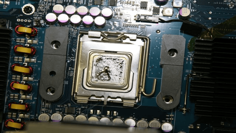 Primer plano de un zócalo de CPU en la placa base de una computadora, con residuos de pasta térmica visibles
