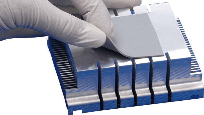 Thermal pad installation: Gloved hand placing a gray thermal pad onto a silver aluminum heat sink, designed for heat dissipation in electronic components (CPU, GPU) in computing or industrial electronics