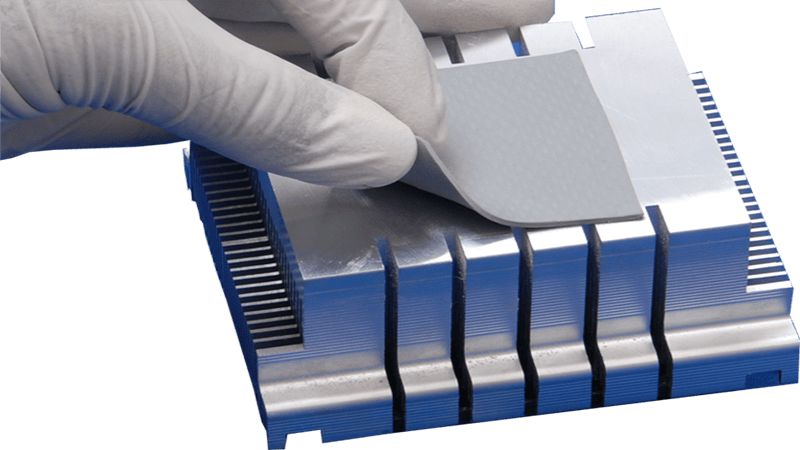 Thermal pad installation: Gloved hand placing a gray thermal pad onto a silver aluminum heat sink, designed for heat dissipation in electronic components (CPU, GPU) in computing or industrial electronics
