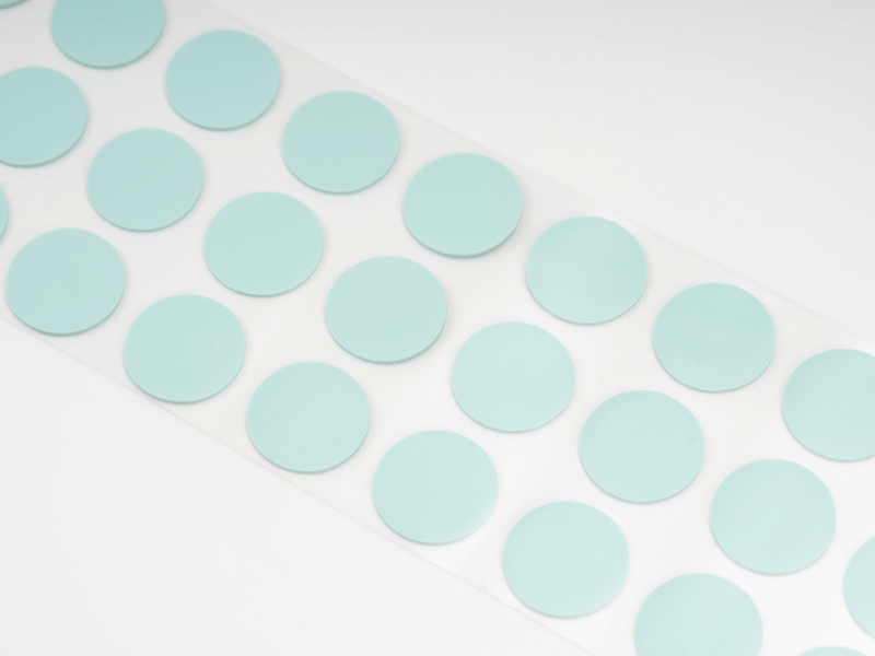 Almohadilla precortada de material de interfaz térmica (TIM) Jiuju de color verde pálido sobre una lámina protectora.