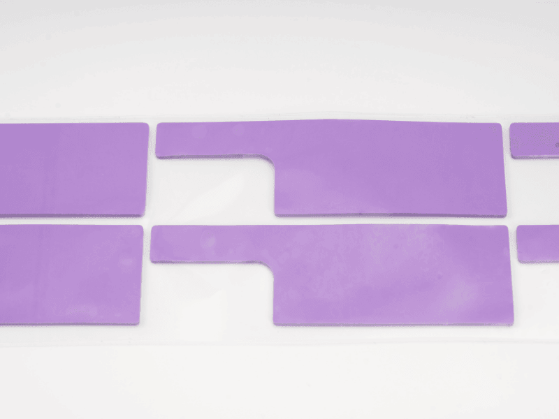 Almohadilla de material de interfaz térmica (TIM) Jiuju puro de color pálido, precortada sobre un revestimiento protector.