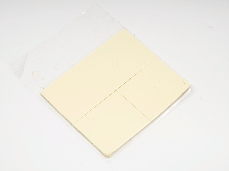 Almohadilla de material de interfaz térmica (TIM) Jiuju de color amarillo pálido precortada sobre una lámina protectora.