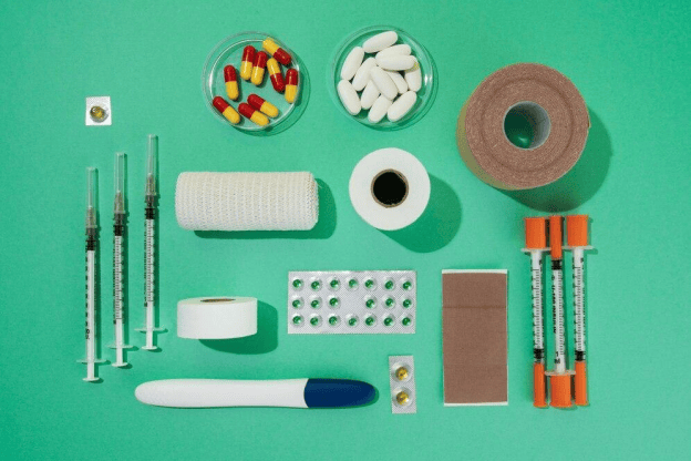 Syringes and medicines have been arranged on a green background board with rolls of gauze.