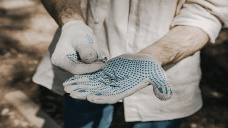 Worker wearing blue and white gloves showing the screw in his hand